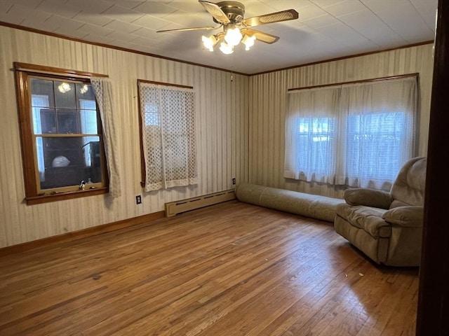 living area with crown molding, a baseboard heating unit, hardwood / wood-style floors, and ceiling fan