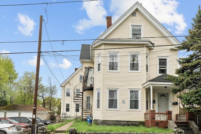 view of front of house with a chimney, a balcony, and roof with shingles