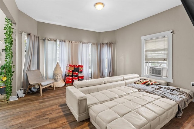 living area with cooling unit, a baseboard heating unit, a wealth of natural light, and wood finished floors