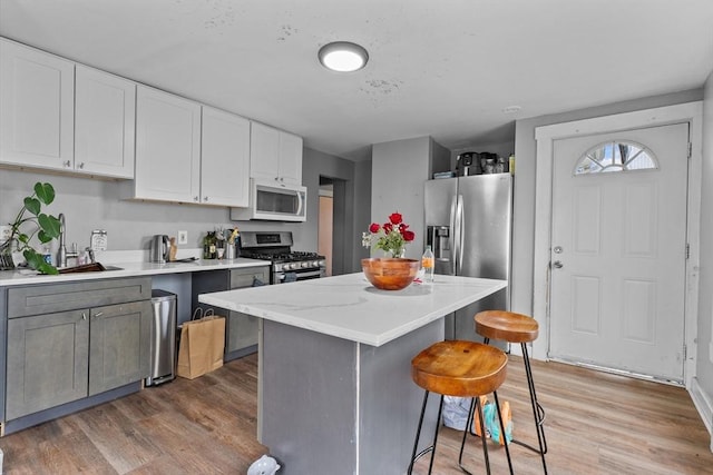kitchen with a breakfast bar, light wood finished floors, stainless steel appliances, white cabinetry, and a kitchen island