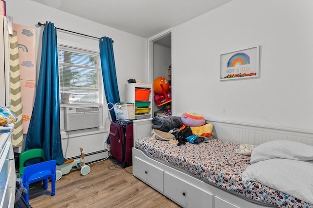 bedroom featuring cooling unit, a baseboard heating unit, light wood-style flooring, and a wainscoted wall