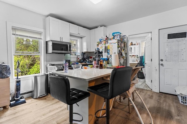 kitchen with white cabinets, light stone counters, light wood finished floors, a kitchen breakfast bar, and stainless steel microwave