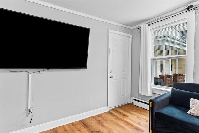 living area featuring baseboards, light wood-style flooring, crown molding, and a baseboard heating unit