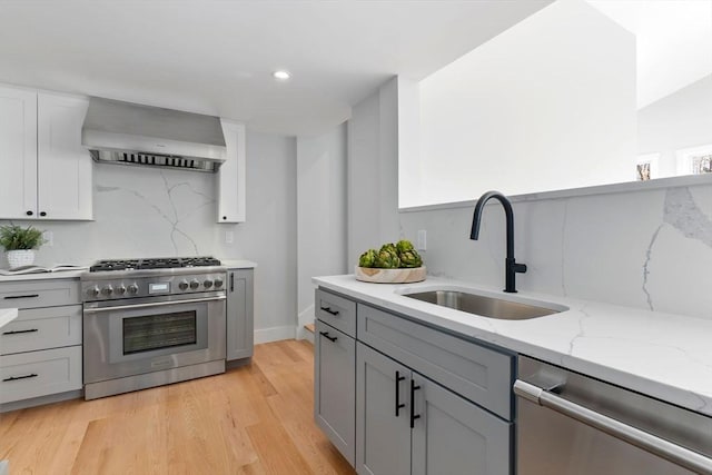 kitchen with wall chimney exhaust hood, sink, light hardwood / wood-style flooring, stainless steel appliances, and light stone countertops