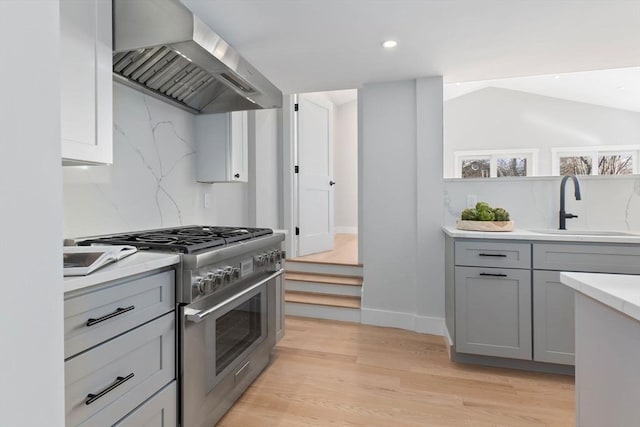 kitchen featuring sink, gray cabinetry, high end stainless steel range oven, exhaust hood, and light wood-type flooring