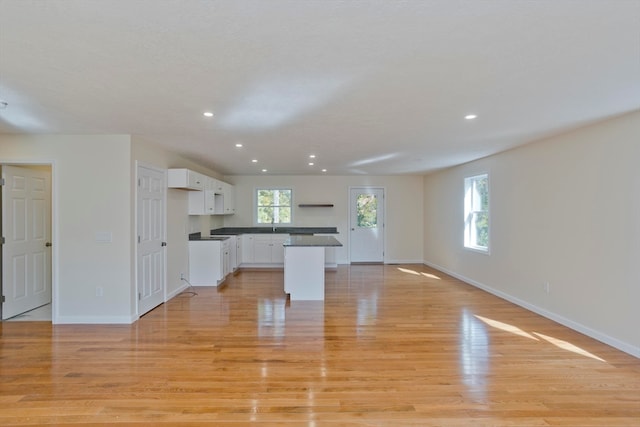 kitchen with light wood-type flooring, white cabinets, a kitchen island, and a wealth of natural light