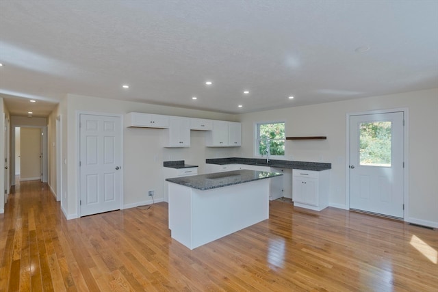 kitchen with light hardwood / wood-style floors, a center island, a textured ceiling, white cabinetry, and dark stone countertops