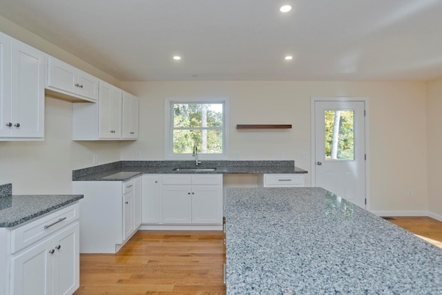 kitchen with light wood-type flooring, stone counters, sink, and white cabinets