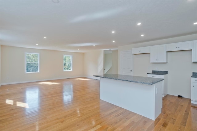 kitchen with light hardwood / wood-style floors, stone counters, a center island, and white cabinets