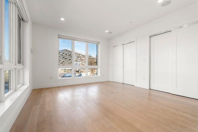 unfurnished bedroom featuring light wood-style flooring, recessed lighting, and multiple closets