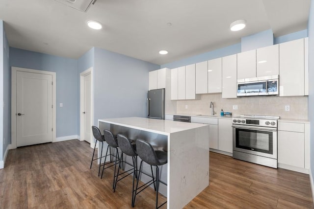 kitchen featuring dark wood-type flooring, white cabinetry, a kitchen island, a breakfast bar, and stainless steel appliances