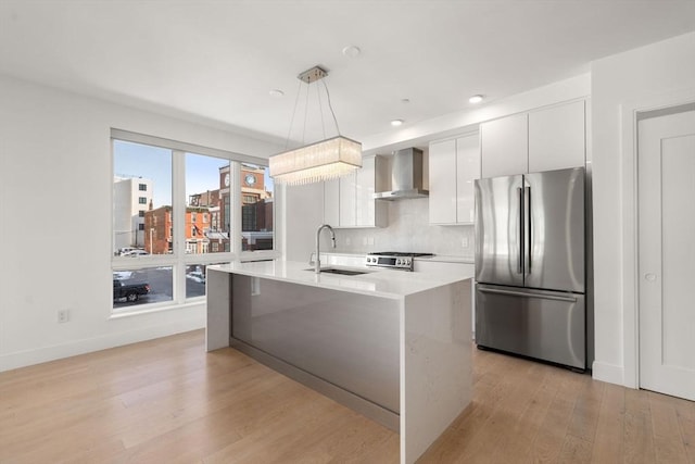 kitchen featuring white cabinets, wall chimney exhaust hood, a sink, light countertops, and stainless steel appliances