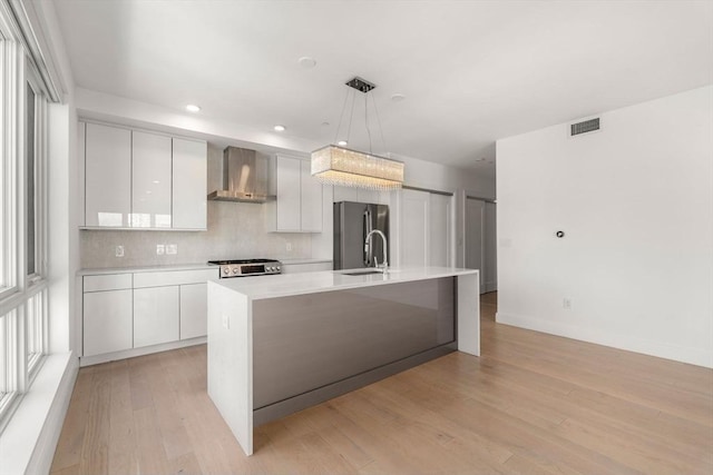 kitchen featuring wall chimney range hood, light countertops, freestanding refrigerator, white cabinetry, and modern cabinets