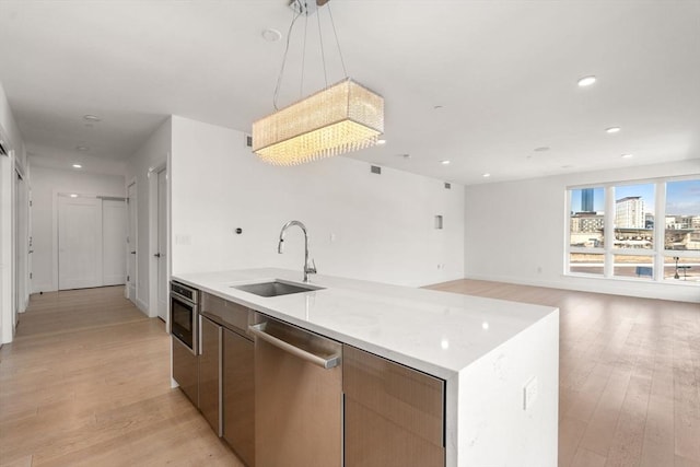 kitchen featuring light wood-type flooring, a kitchen island with sink, appliances with stainless steel finishes, pendant lighting, and a sink