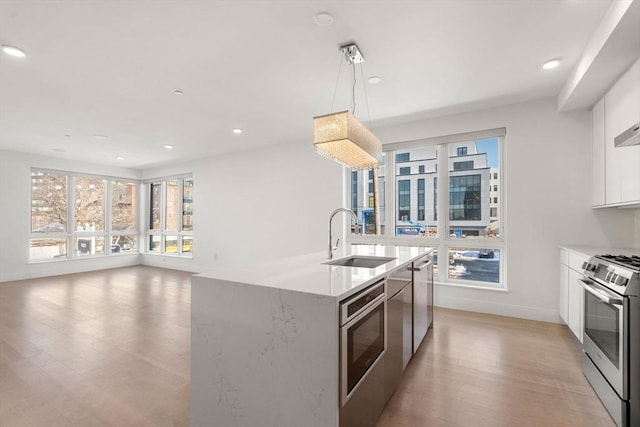 kitchen featuring stainless steel range with gas stovetop, light wood-type flooring, white cabinets, recessed lighting, and a sink