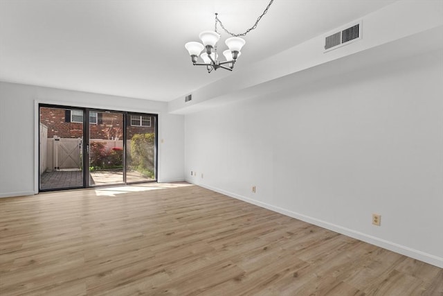 spare room with a chandelier, wood finished floors, and baseboards