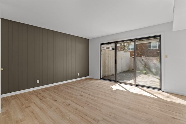 empty room featuring light wood-style floors, baseboards, and wood walls