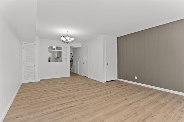 unfurnished living room with a chandelier, light wood finished floors, and baseboards