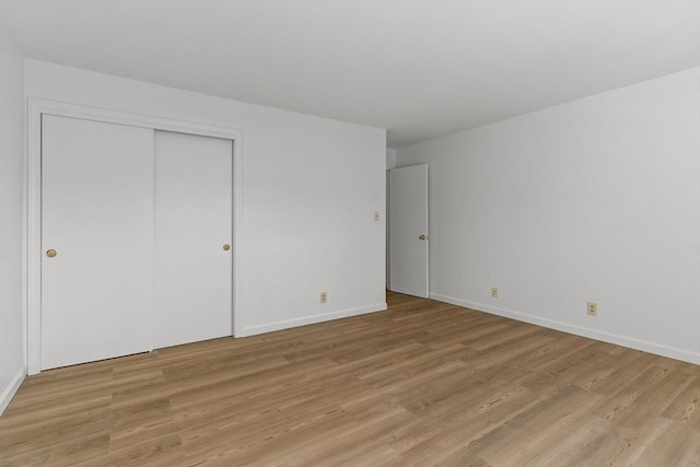 unfurnished bedroom featuring light wood-style floors, baseboards, and a closet