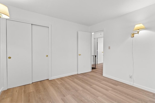 unfurnished bedroom with light wood-style flooring, baseboards, and a closet