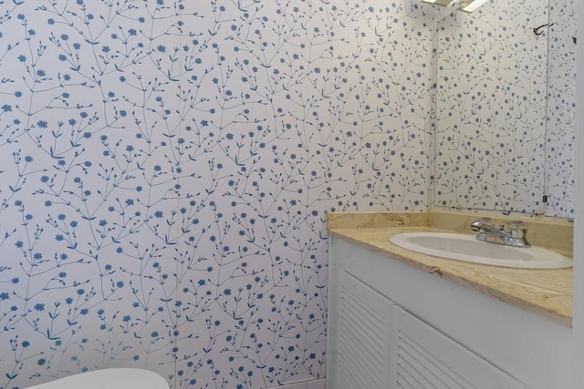 bathroom featuring vanity, wallpapered walls, and toilet
