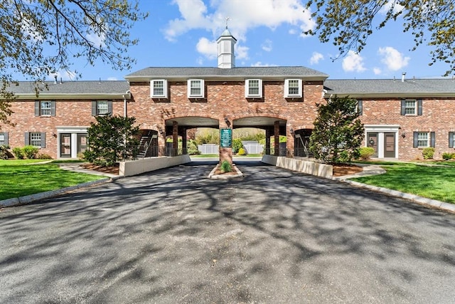 view of property with a carport, brick siding, a front yard, and driveway