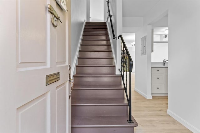 staircase featuring wood finished floors, baseboards, and electric panel