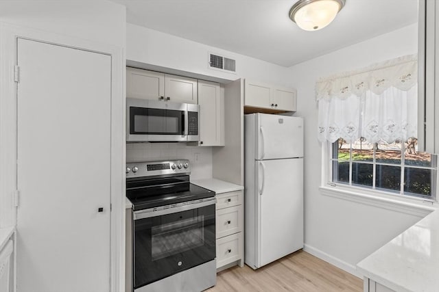 kitchen featuring stainless steel appliances, light wood-style floors, tasteful backsplash, baseboards, and white cabinetry