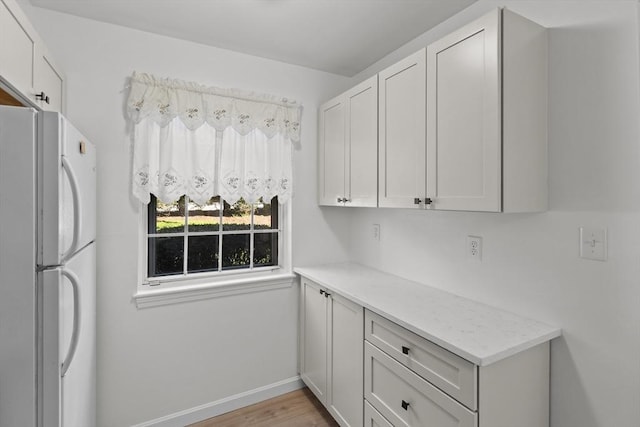 kitchen with freestanding refrigerator, light wood-style flooring, baseboards, light stone countertops, and white cabinets