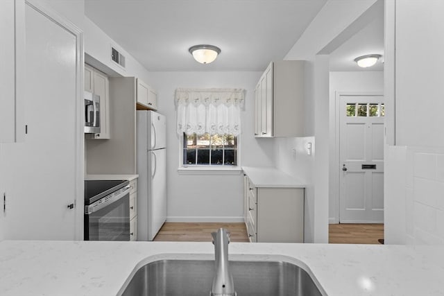 kitchen featuring stainless steel appliances, a sink, light wood-type flooring, light stone counters, and baseboards