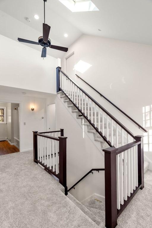 stairs featuring a skylight, ceiling fan, carpet floors, and high vaulted ceiling