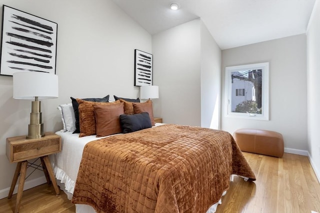 bedroom with baseboards, light wood finished floors, and lofted ceiling