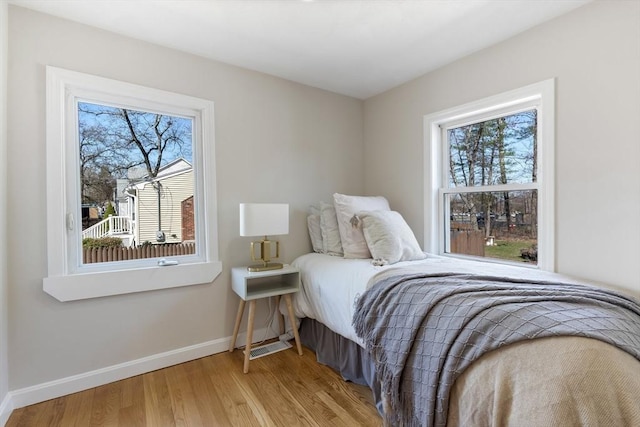 bedroom with baseboards, multiple windows, and wood finished floors