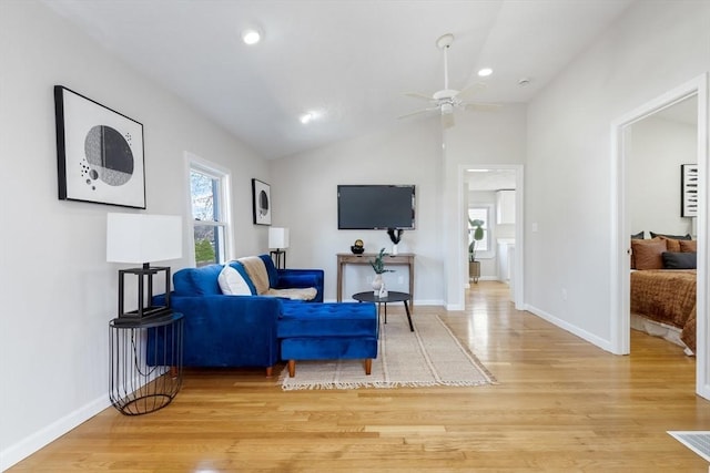 living area with baseboards, ceiling fan, light wood-type flooring, and lofted ceiling