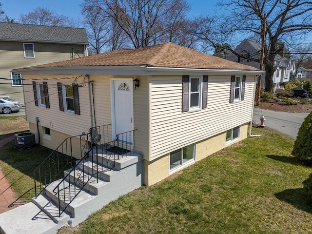 view of front of house with a front lawn, roof with shingles, and central AC
