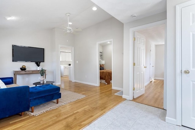 living area featuring baseboards, a ceiling fan, and light wood finished floors