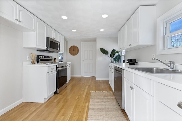 kitchen with baseboards, a sink, light wood-style floors, and stainless steel appliances