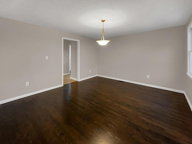 spare room with baseboards and dark wood-type flooring