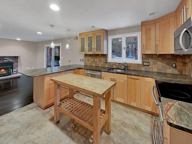 kitchen featuring light brown cabinetry, appliances with stainless steel finishes, a brick fireplace, a sink, and a peninsula