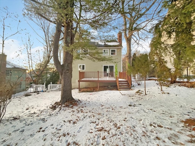 snow covered rear of property with a chimney, fence, and a deck