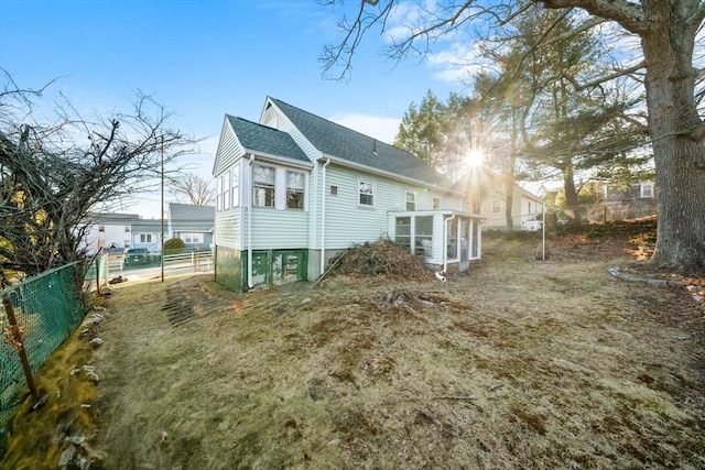 rear view of property featuring a shingled roof, a sunroom, and fence