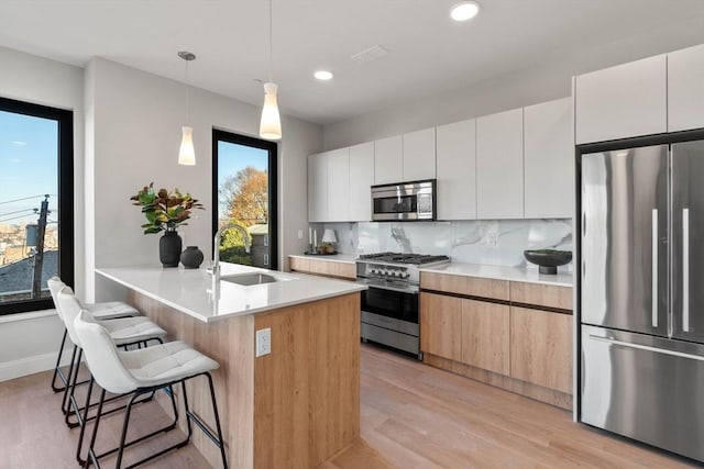 kitchen featuring stainless steel appliances, a sink, a breakfast bar area, modern cabinets, and recessed lighting
