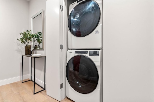 clothes washing area with estacked washer and dryer, light wood-type flooring, and baseboards
