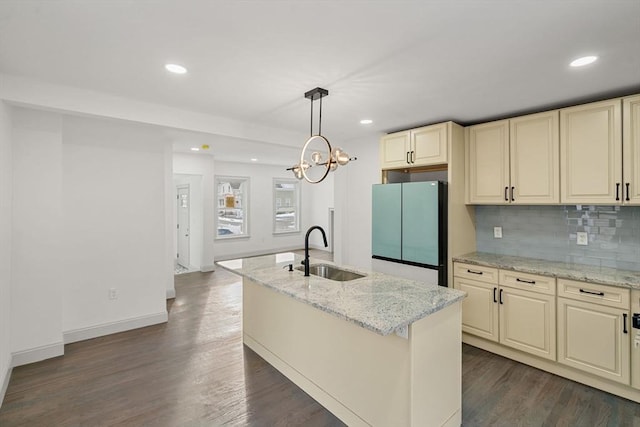 kitchen featuring light stone counters, sink, fridge, and a center island with sink