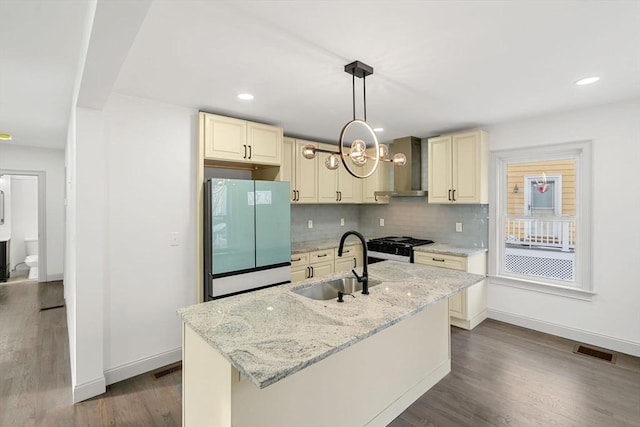 kitchen with refrigerator, an island with sink, pendant lighting, black gas range, and wall chimney range hood