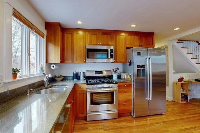 kitchen featuring brown cabinets, stainless steel appliances, light wood-style floors, and a sink