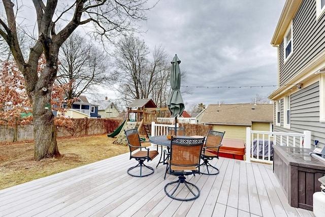 deck featuring outdoor dining area, a fenced backyard, and a playground