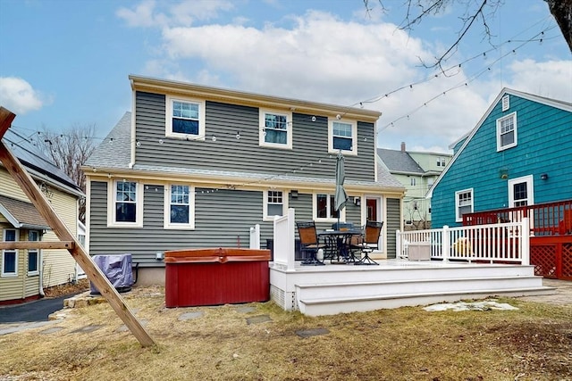 rear view of property with a deck and a hot tub