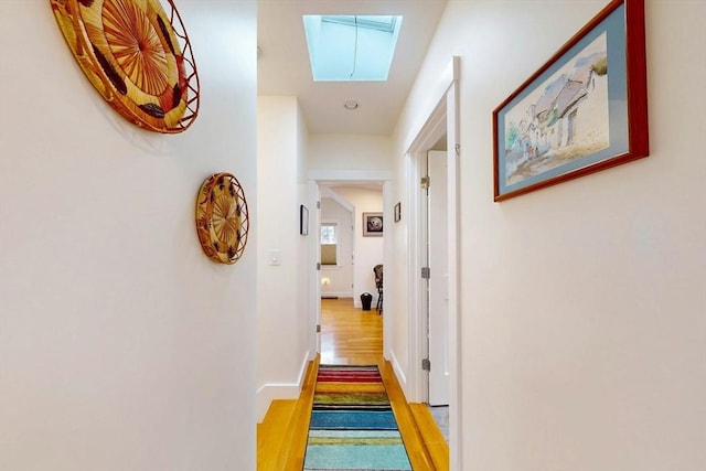 corridor with a skylight, wood finished floors, and baseboards