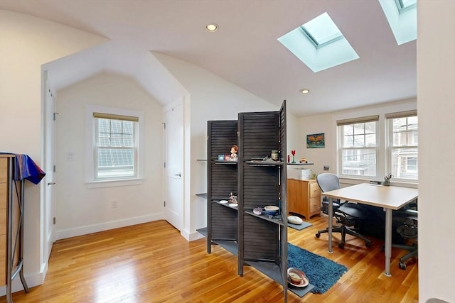 office area featuring vaulted ceiling with skylight, light wood-type flooring, and a healthy amount of sunlight